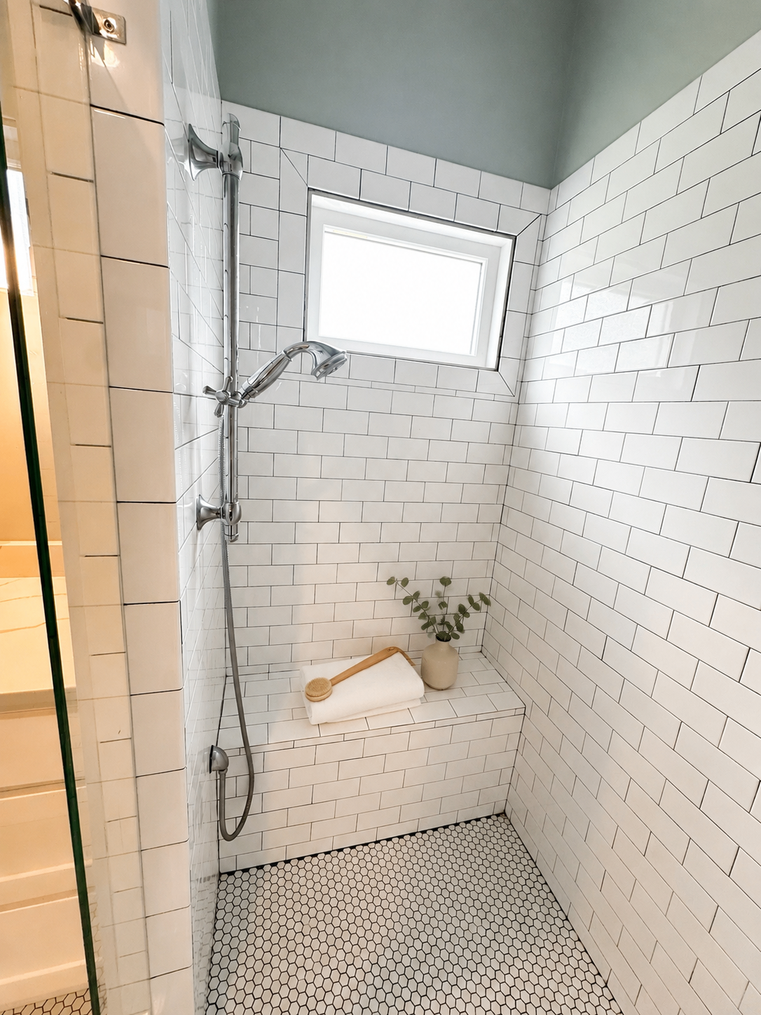 Walk-in shower with built-in bench, window, and subway tile surround